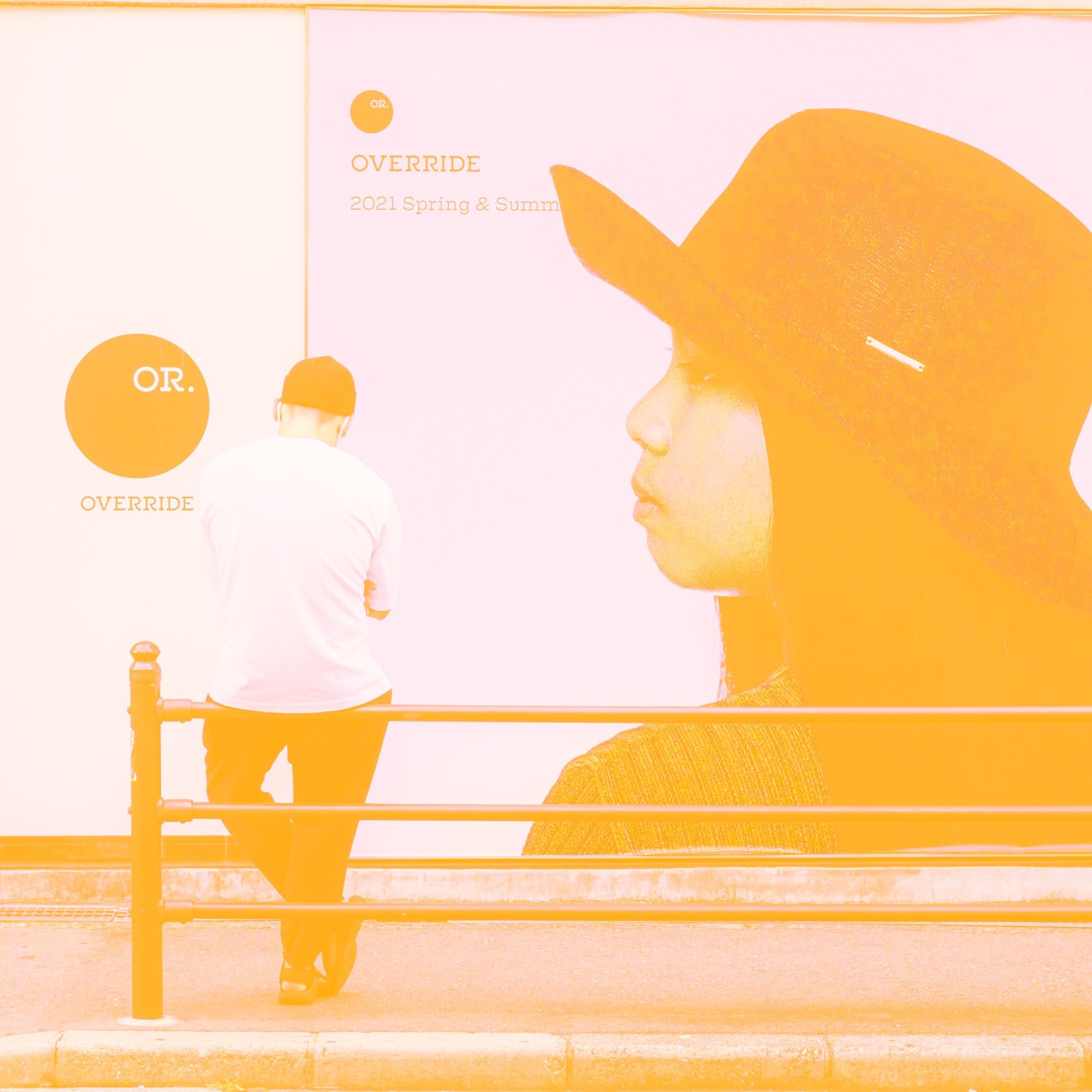 person standing next to override brand poster on street amber toned