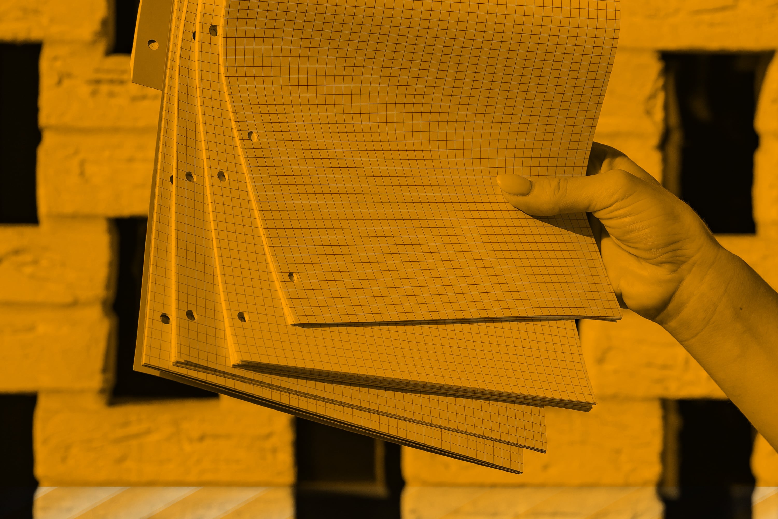 hand holding stack of graph paper notepad pages amber toned