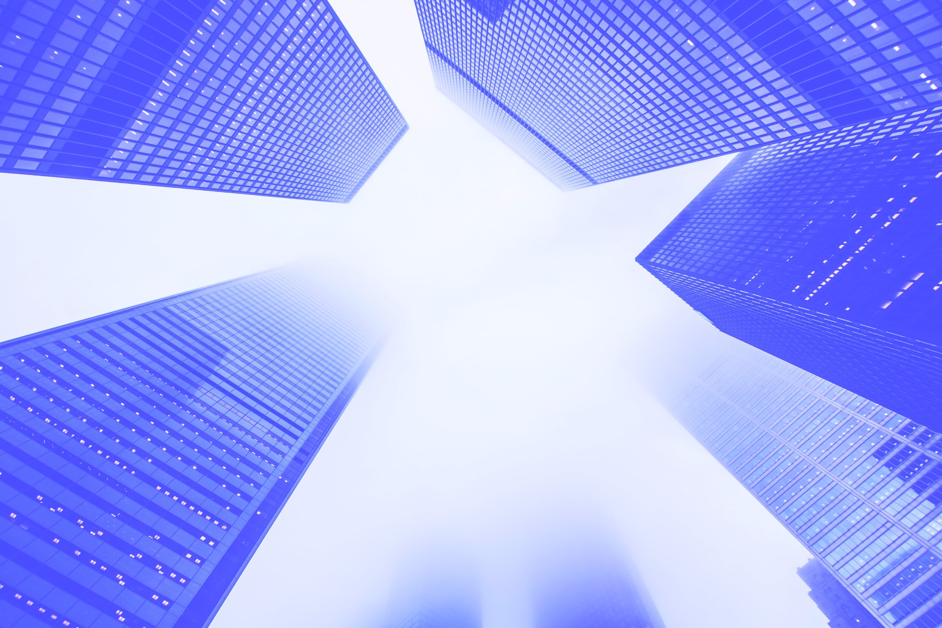 looking up at tall glass skyscrapers converging in fog blue toned