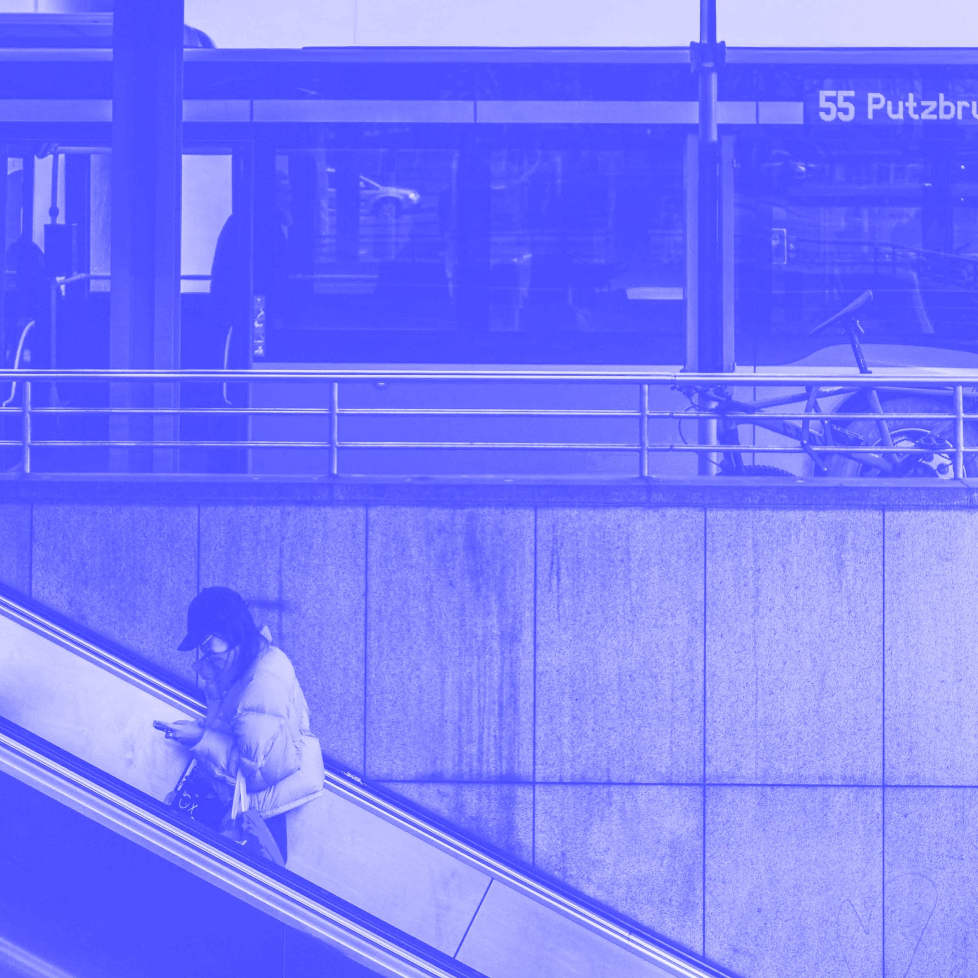 woman on escalator using smartphone with bus in background blue toned
