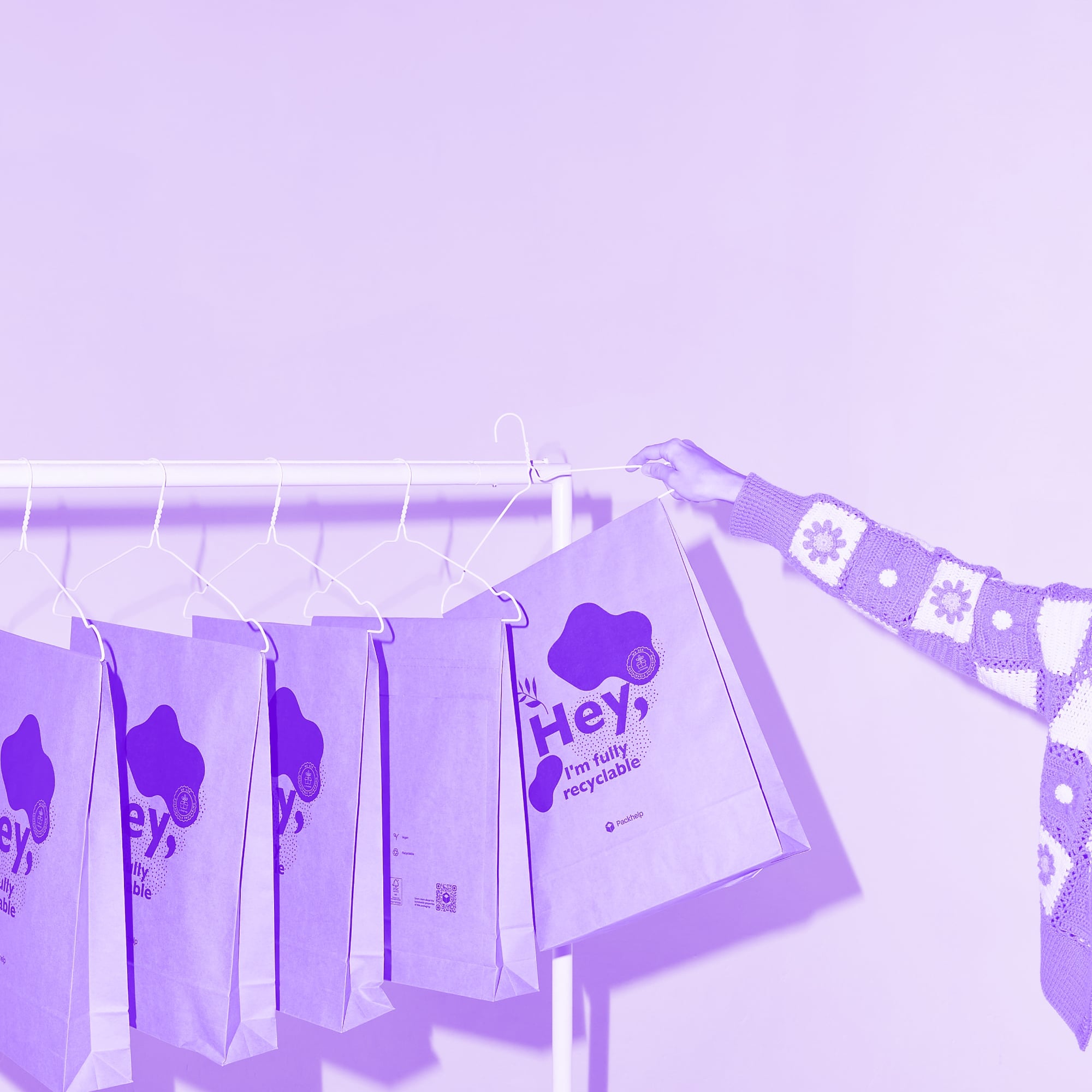 branded recyclable paper bags hanging on clothing rail with hand reaching purple