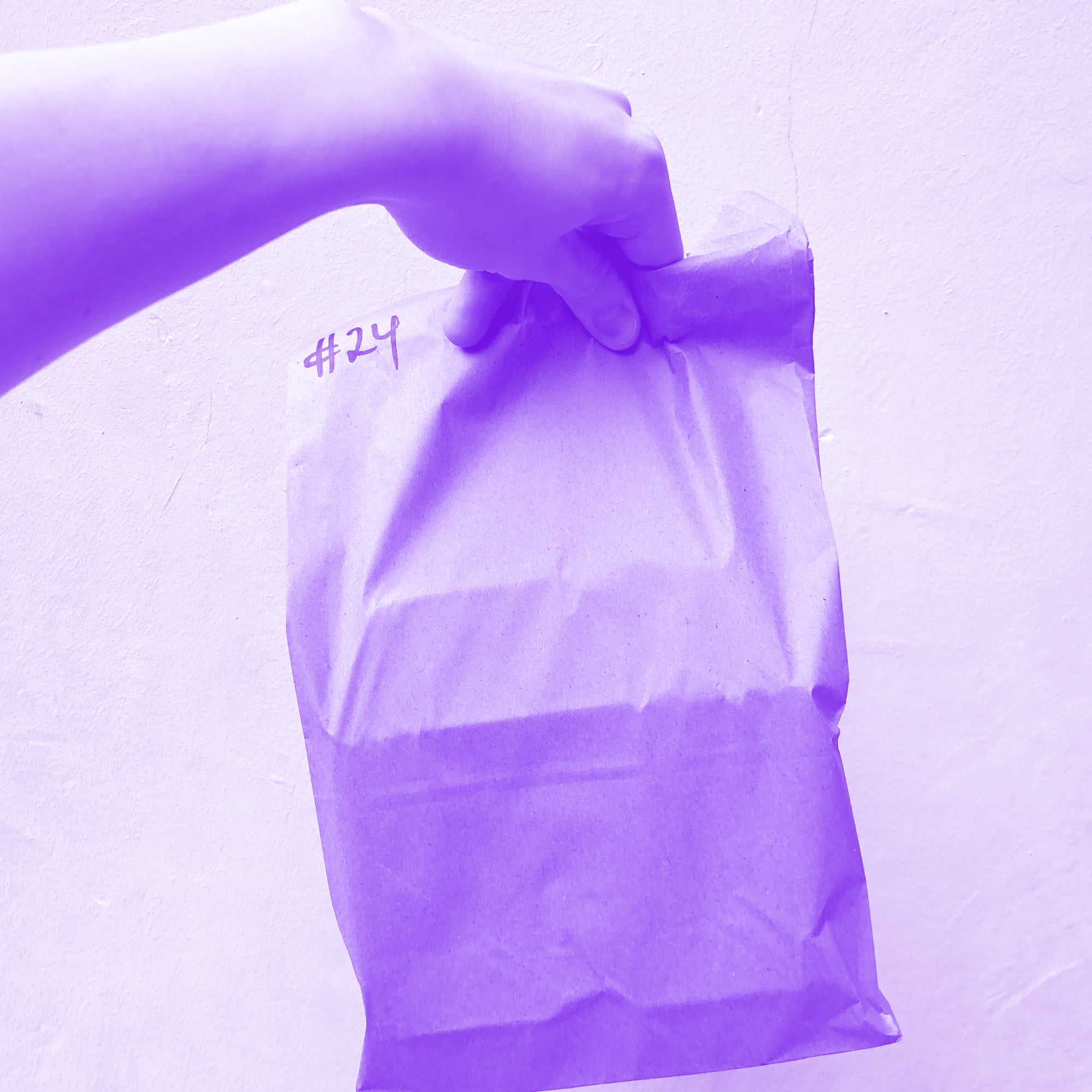 hand holding plain brown paper delivery bag with number 24 purple toned