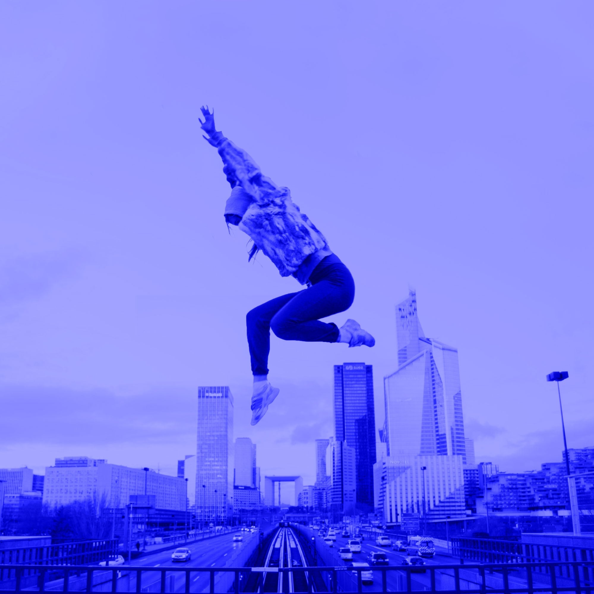 woman jumping high in mid air against city skyline with skyscrapers blue toned
