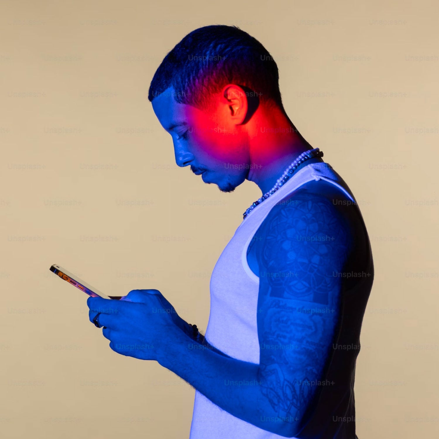 tattooed man with shaved head browsing smartphone side profile red and blue neon lighting