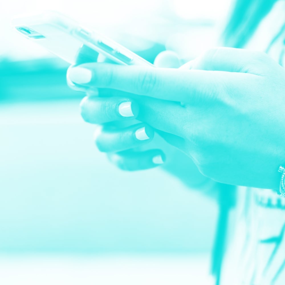 close up of hands holding and typing on smartphone next to bicycle teal toned