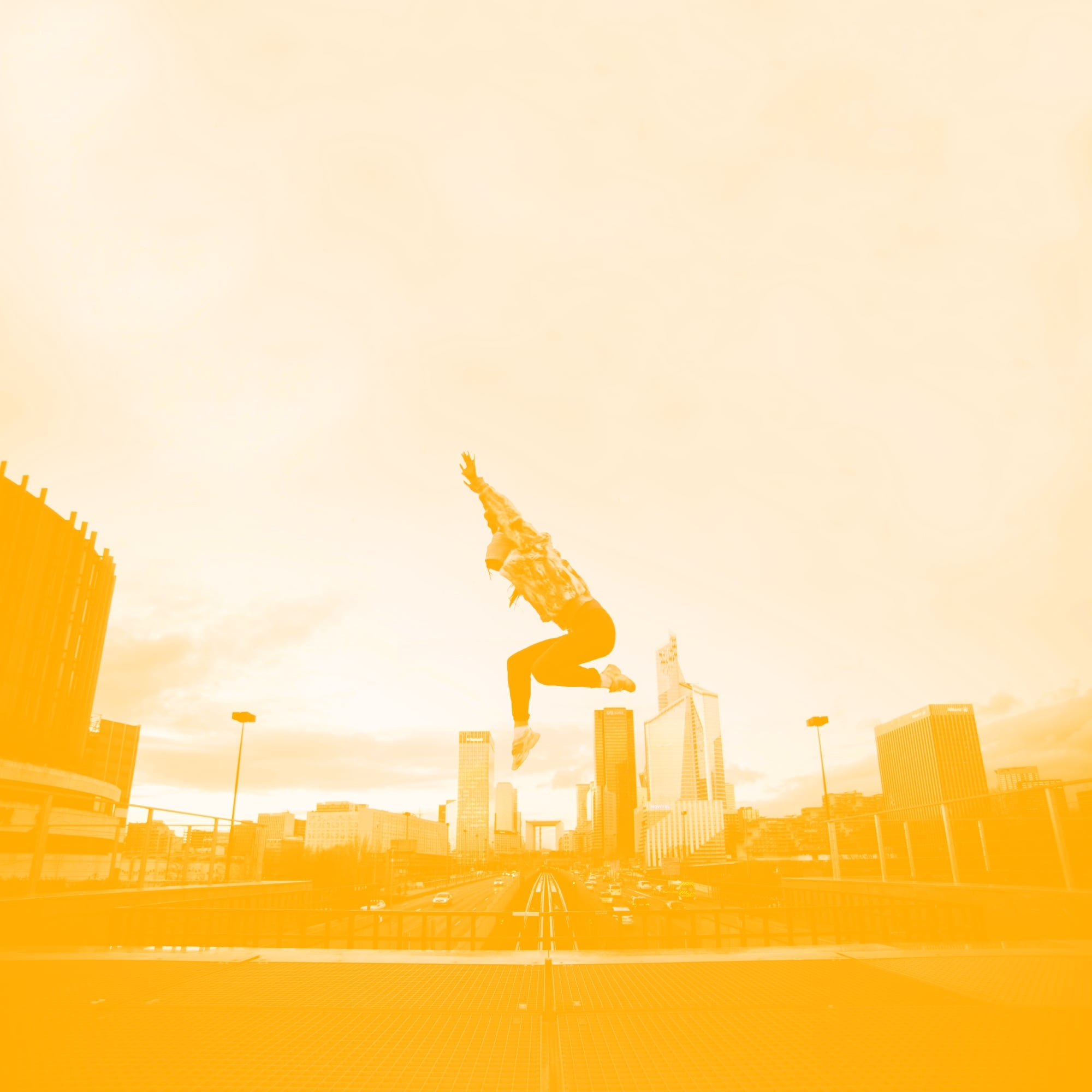 woman jumping high above city skyline with arms raised golden amber toned