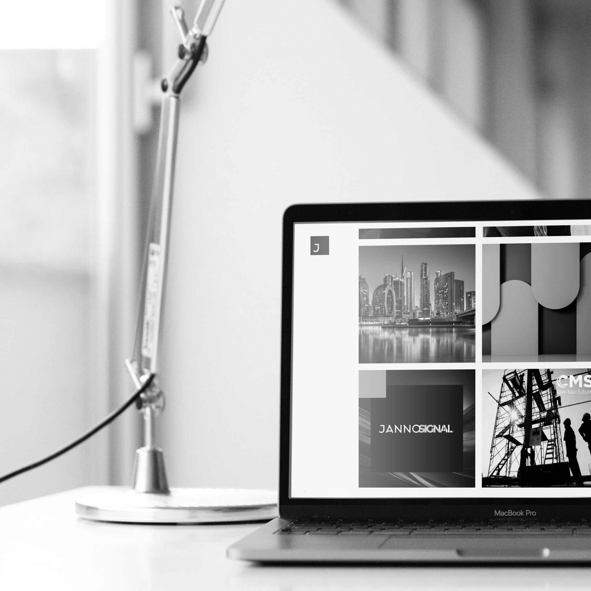 macbook pro on desk showing portfolio website grid with desk lamp black and white