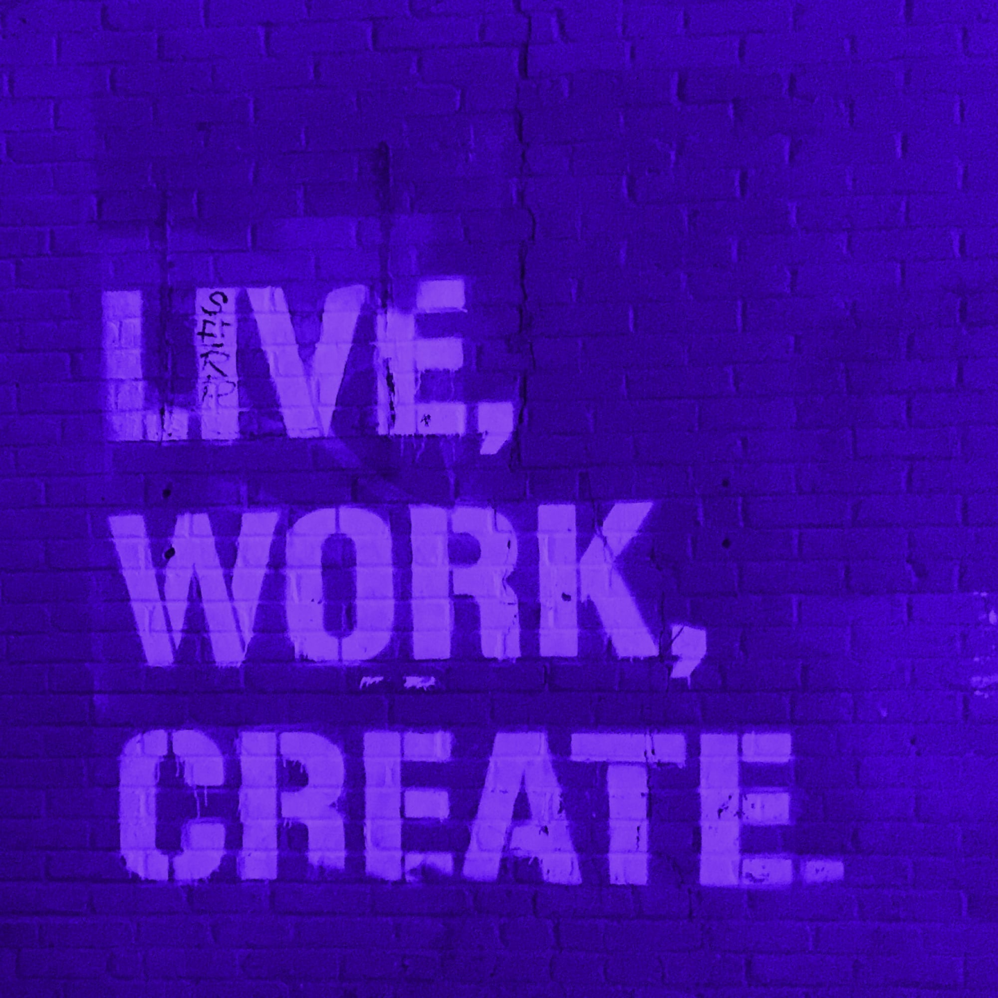 live work create stencil graffiti text on brick wall purple toned