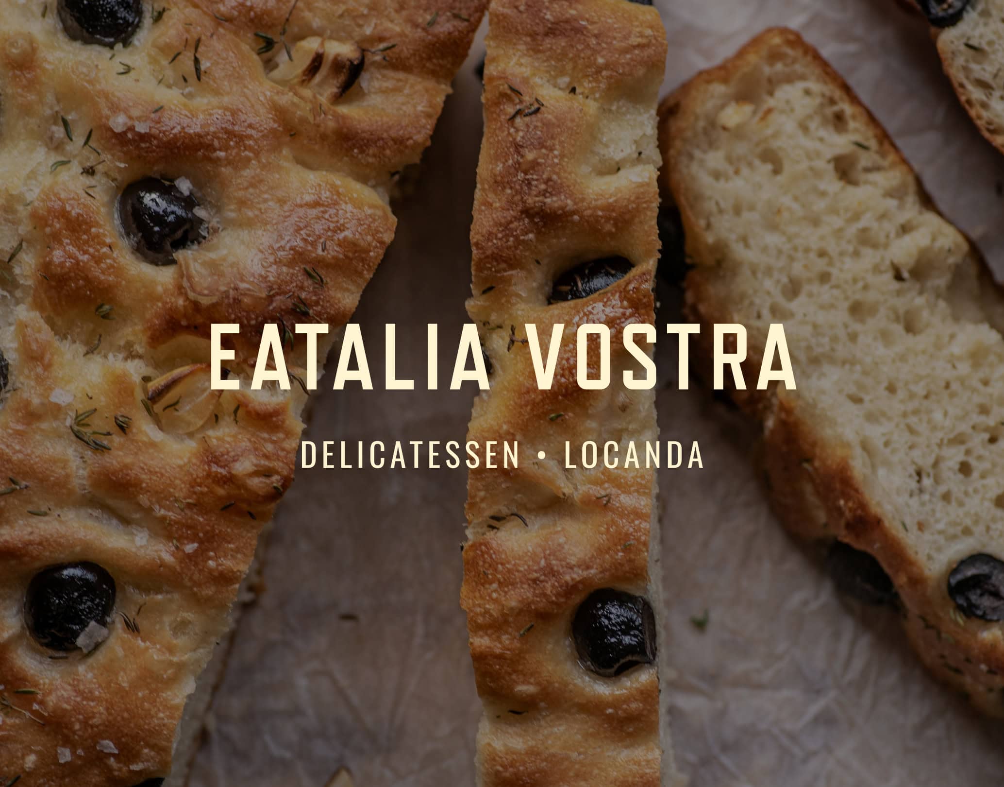 Eatalia Vostra wordmark over sliced olive focaccia sprinkled with herbs on baking paper
