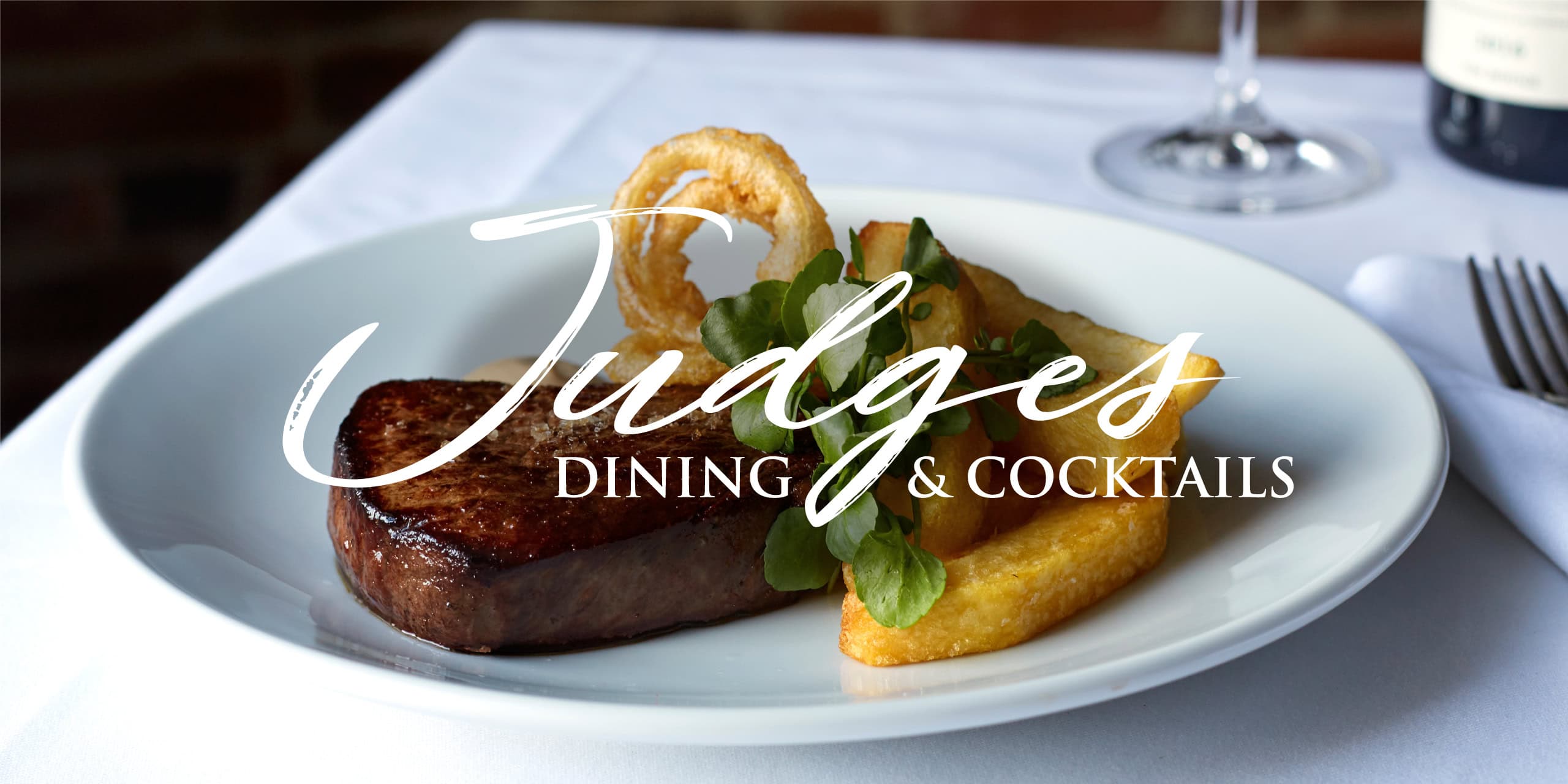 Steak with chips, onion ring and watercress on a white plate, overlaid with Judges Dining & Cocktails