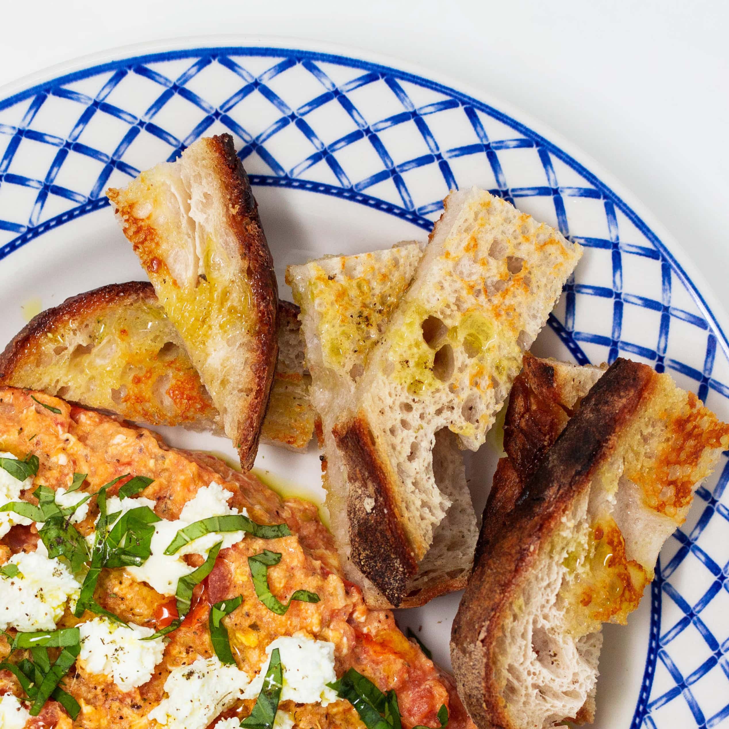 Greek dip topped with feta and herbs served with toasted bread on a blue patterned plate