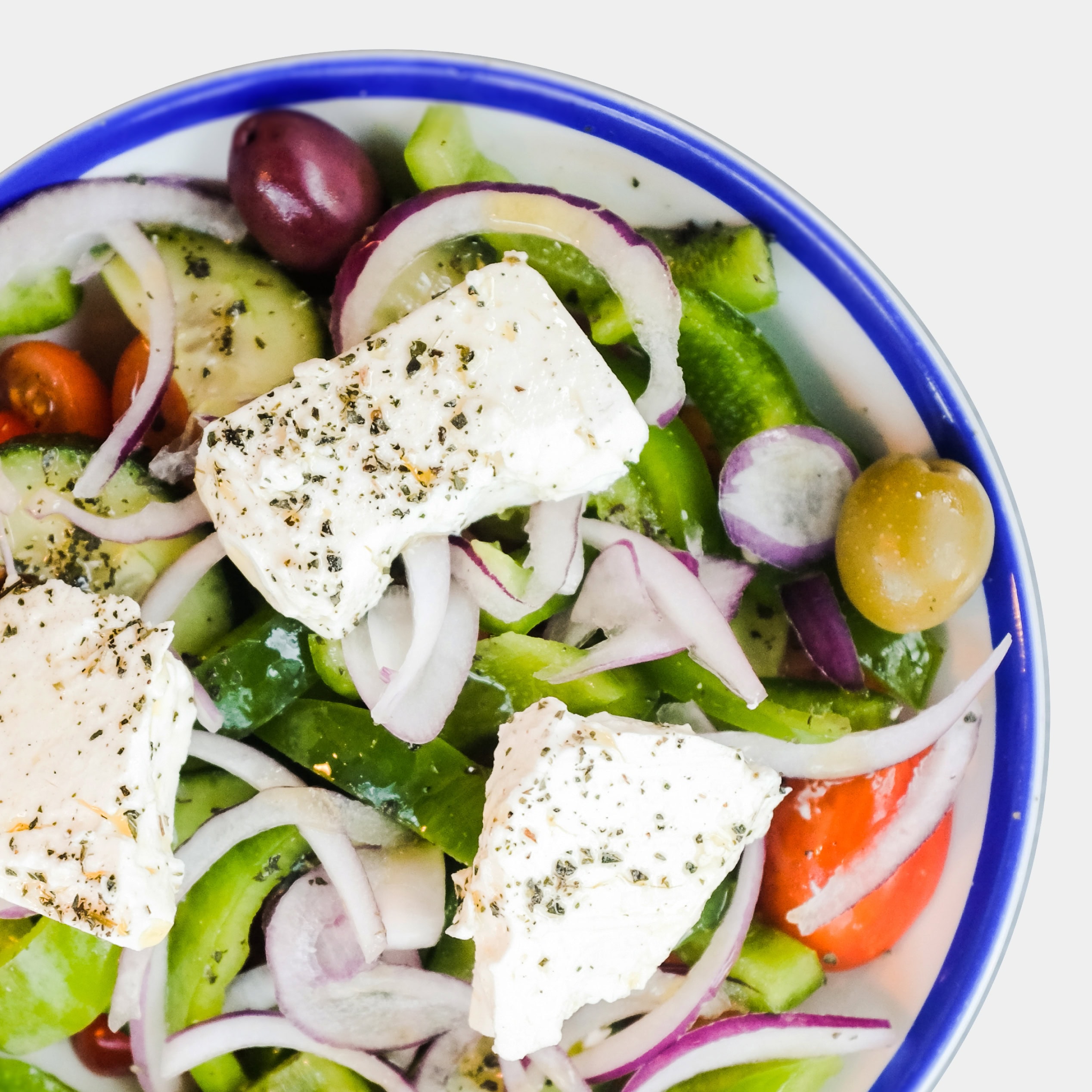 Greek salad with feta, cucumber, tomato, red onion and olives in a white bowl with a blue rim