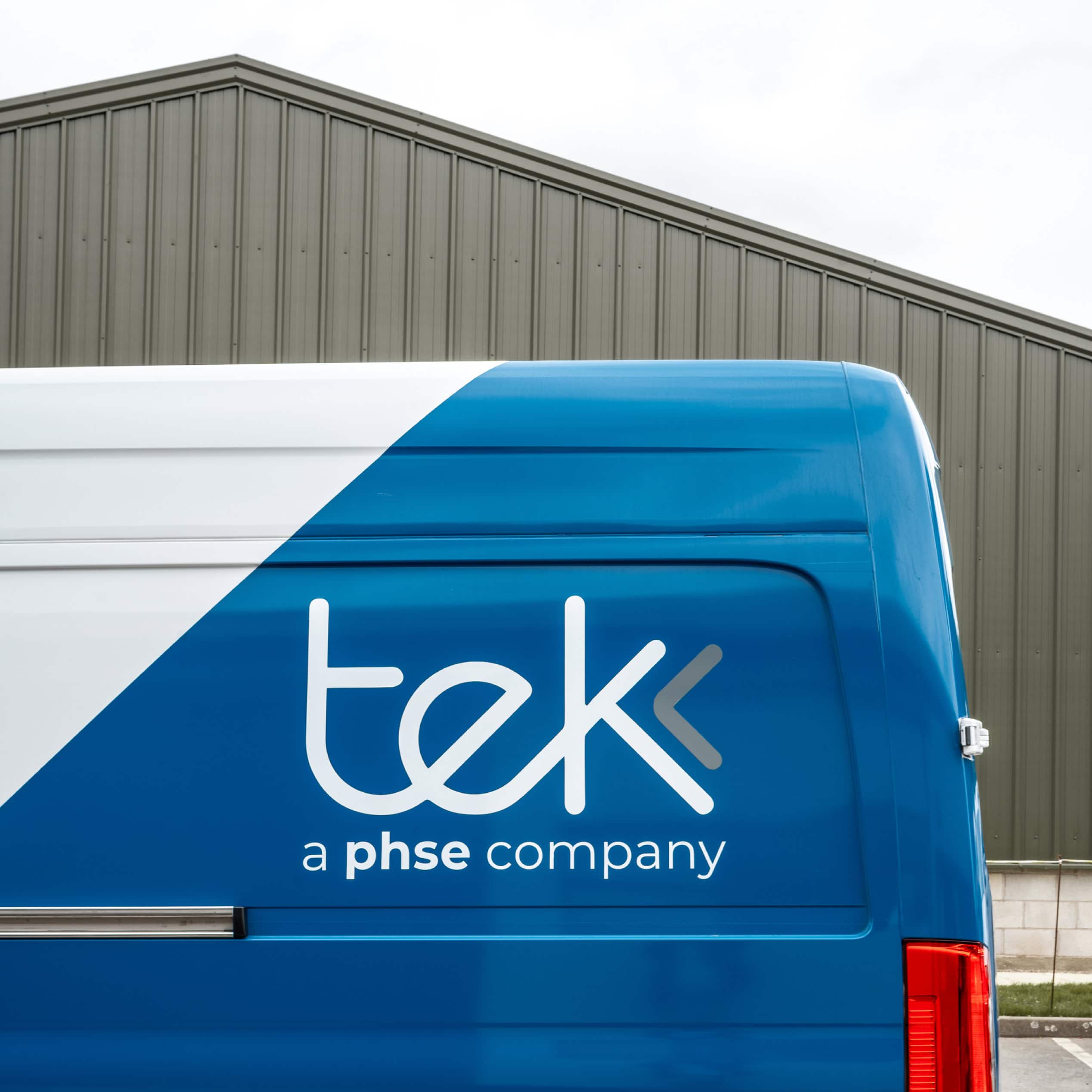 Tek logo on the side of a blue delivery van outside a warehouse